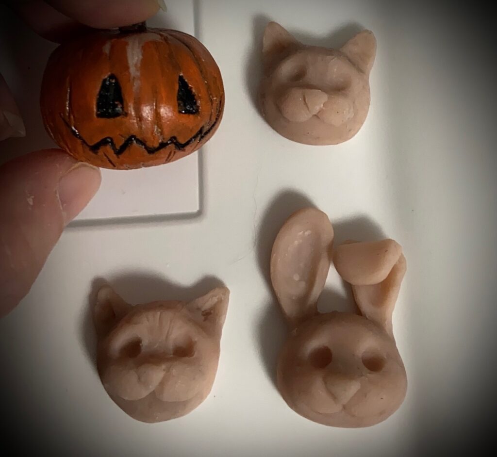 Vier kleine Figuren aus Sculpy-Clay. Ein Kürbis eingefärbt und drei flache, kleine Tierköpfe, die für Kinder-Haarklammern gedacht sind (zwei Katzen und ein Hase).